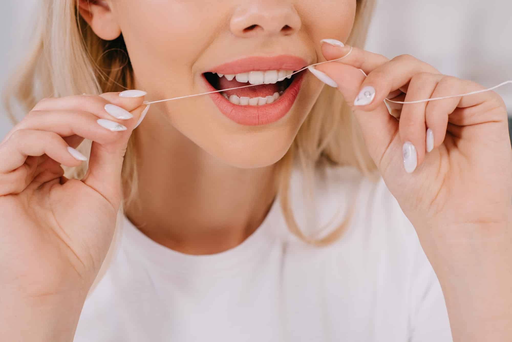 cropped view of woman flossing teeth with dental floss